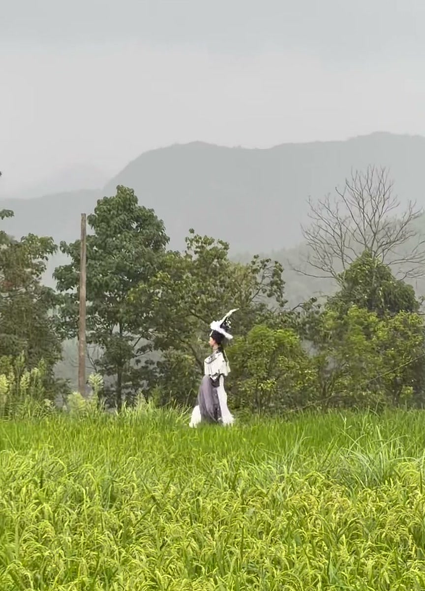 A model in a white feathered headdress, walking the paddy-field runway as rain moved in over the hills